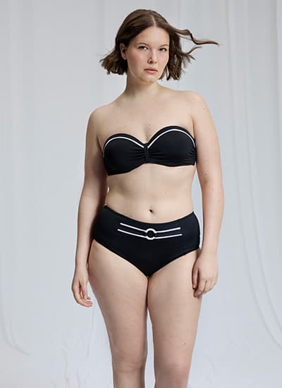 Personne debout de face portant un bikini noir bandeau à détails blancs, devant un fond clair uni