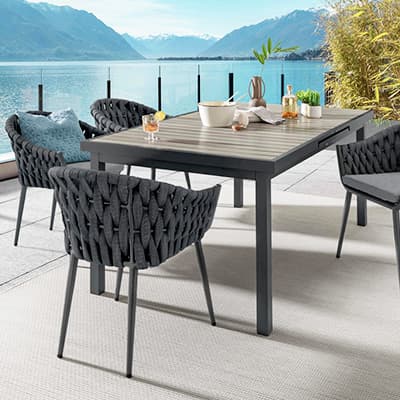 Outdoor-Essbereich mit Blick auf einen See und Berge, Tisch und geflochtene Stühle, sonniges Wetter