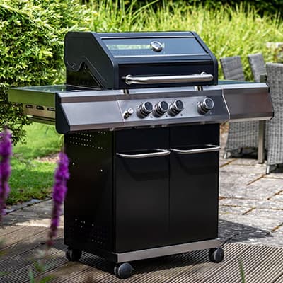 Schwarzer Gasgrill mit vier Reglern und zwei Türen steht auf einer Terrasse im Garten.