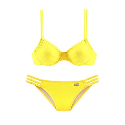 Frau trägt schwarzen Mantel, schwarzes Oberteil und beige Hose mit Gürtel vor weißem Hintergrund