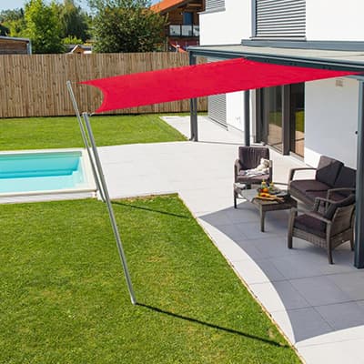 Terrasse moderne avec mobilier de jardin sous une grande toile rouge, piscine à proximité et gazon verdoyant.