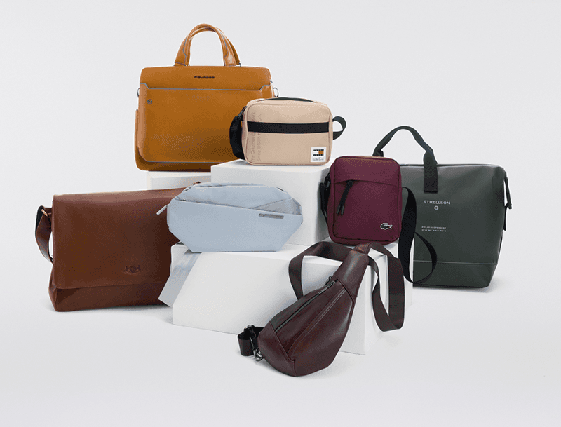 Mehrere Herren-Umhänge-, Schulter- und Gürteltaschen in Braun, Beige, Grau, Bordeaux und Dunkelgrün auf weißen Podesten