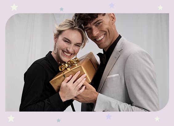 Zwei Personen halten gemeinsam ein goldenes Geschenk, der Hintergrund ist weiß mit pastellfarbenen Sternen.