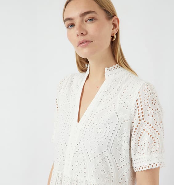 Frau trägt weißes Spitzenoberteil mit V-Ausschnitt und Stehkragen.