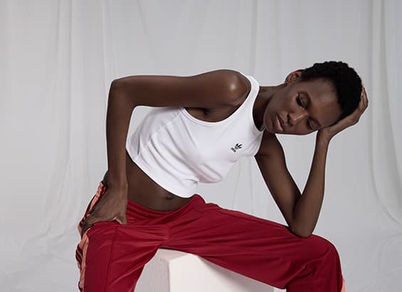 Person in weißem Tanktop und roten Jogginghosen sitzt nachdenklich auf einem weißen Block.