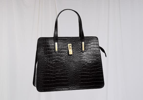 Sac à main noir texturé avec une fermeture dorée, posé devant un fond clair.