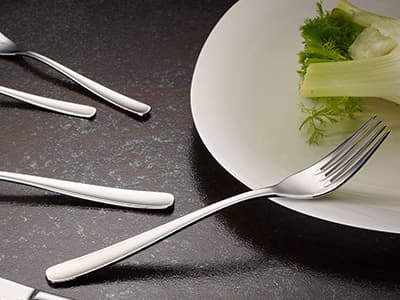 Fourchettes modernes en métal posées sur une table sombre, près d'une assiette blanche avec des légumes verts.