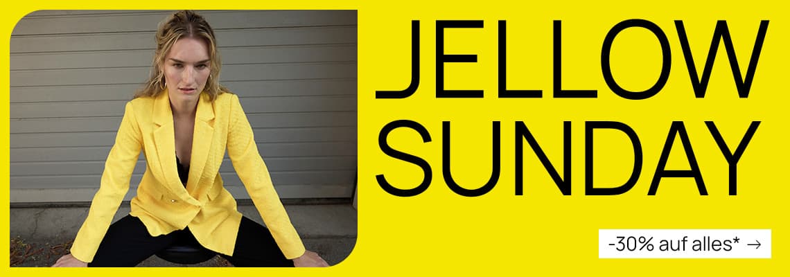 JELLOW SUNDAY – -30 % sur tout* – Person im gelben Blazer sitzt breitbeinig vor grauer Wand