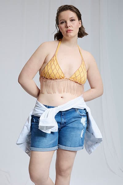 Personne debout portant un soutien-gorge noir, un bijou de corps doré et un pantalon noir transparent