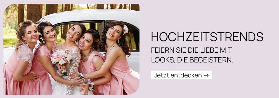 HOCHZEITSTRENDS – Braut mit Blumenstrauß steht lachend mit Freundinnen in rosa Kleidern vor einem Auto