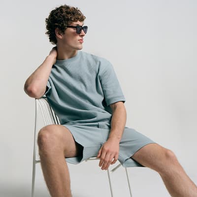 Mann in lockerem T‑Shirt und Shorts sitzt lässig auf einem Stuhl und blickt zur Seite