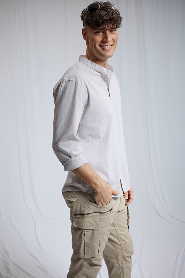 Homme de profil portant chemise à col officier blanche et pantalon cargo beige, main dans la poche