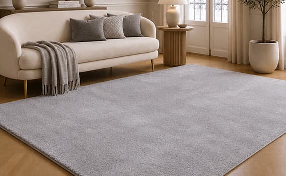Tapis rectangulaire gris clair dans un salon épuré avec canapé beige, coussins assortis et grande fenêtre en arrière-plan