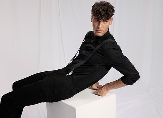 Frau in schwarzer Bluse und glitzerndem Rock kniet auf weißem Boden, trägt schwarze Strumpfhose und Stiefeletten