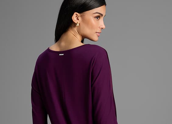 Personne de profil vue de dos portant un haut violet à col rond, fond gris uni
